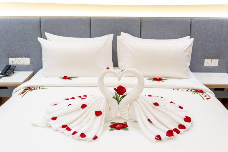 Luxury hotel room for honeymooners: elegant swan towels and scattered rose petals on bed.